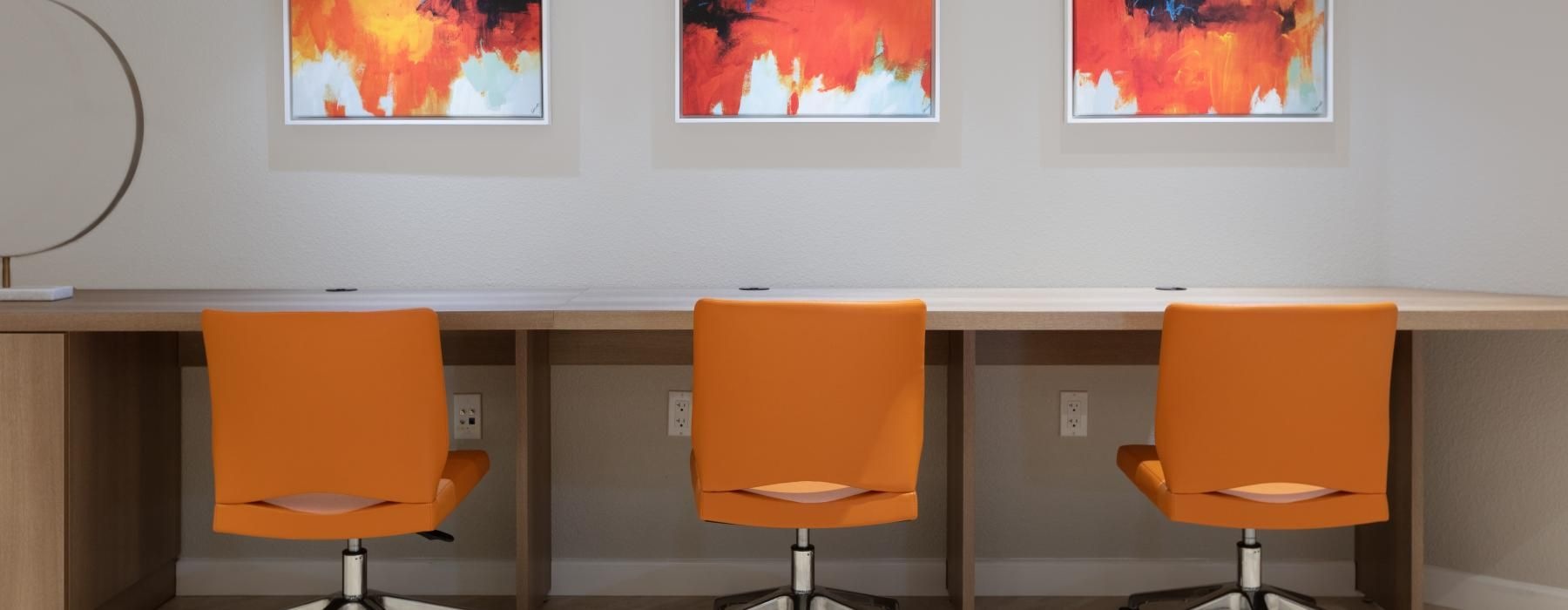 a group of orange chairs in a room with a desk and a wall with art on it