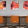 a group of orange chairs in a room with a desk and a wall with art on it